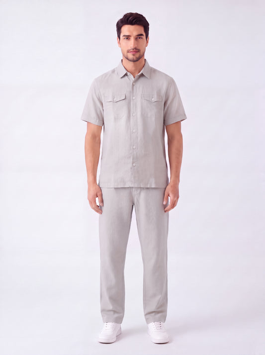 A man modeling a light gray short-sleeve button-up shirt and matching light gray trousers against a plain white studio background.