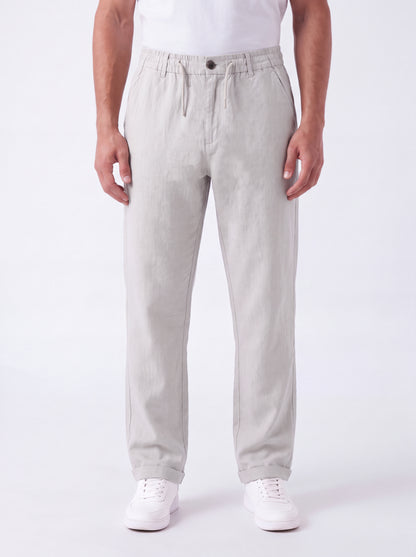 A man wearing light gray drawstring trousers, a white t-shirt, and white sneakers, standing against a plain white studio background.