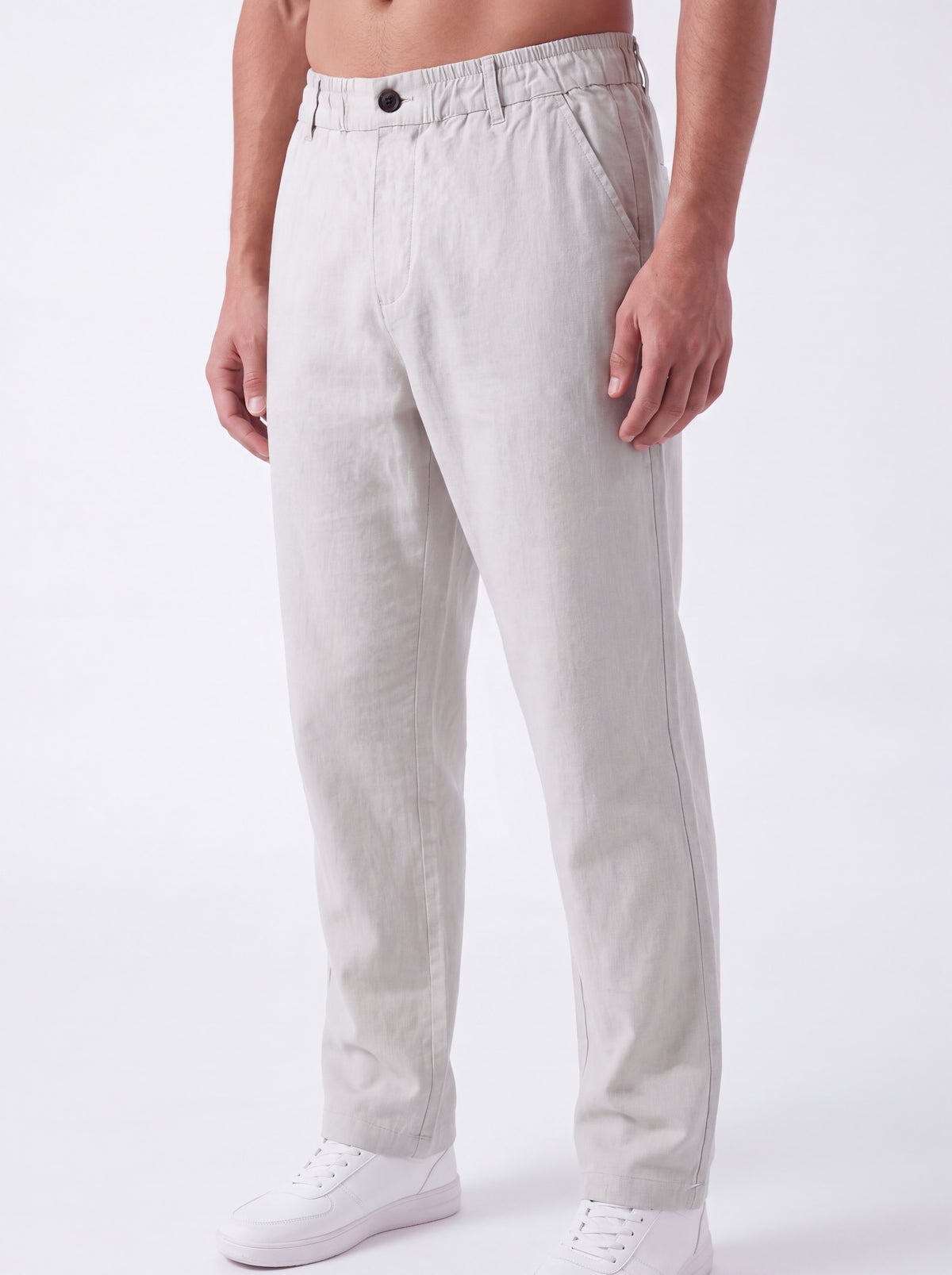 A man wearing light beige linen trousers and white sneakers, shown from the waist down against a plain white studio background.