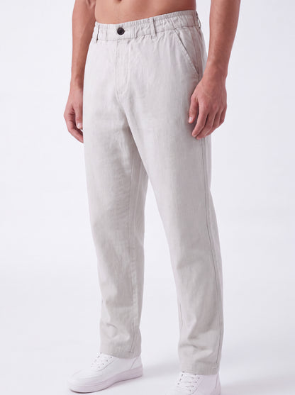 A man wearing light beige linen trousers and white sneakers, shown from the waist down against a plain white studio background.