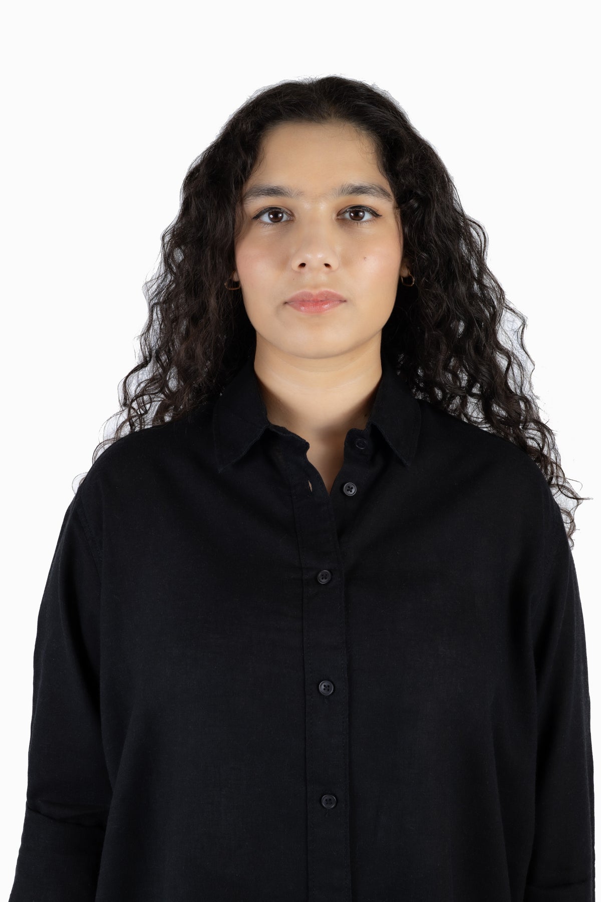 A woman with long, curly dark hair wearing a black button-up shirt, photographed against a solid white background.