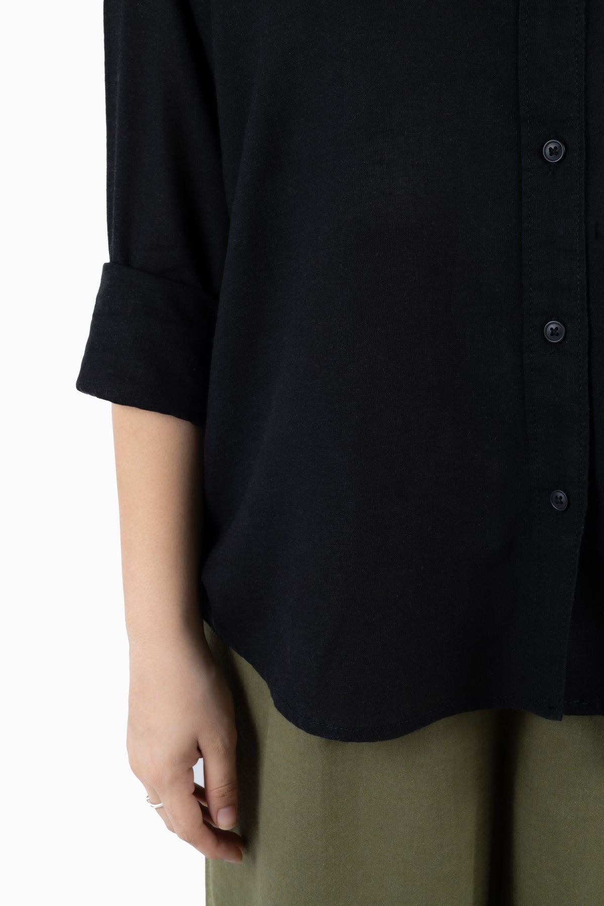 Close-up of a person wearing a black button-front shirt with rolled sleeves and olive green pants against a plain white background.