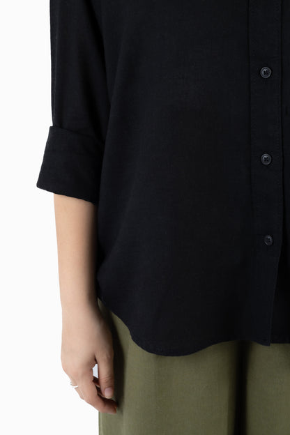 Close-up of a person wearing a black button-front shirt with rolled sleeves and olive green pants against a plain white background.
