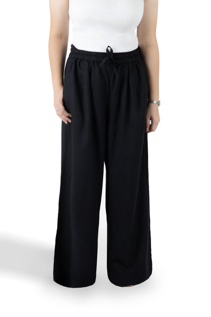 A model wearing black wide-leg drawstring pants and a white sleeveless top, shown from the chest down against a plain white studio background.
