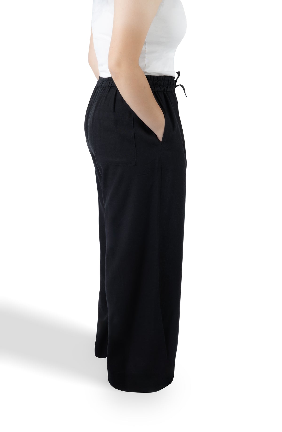 A side profile view of a person wearing black wide-leg drawstring pants and a white sleeveless top against a plain white background.