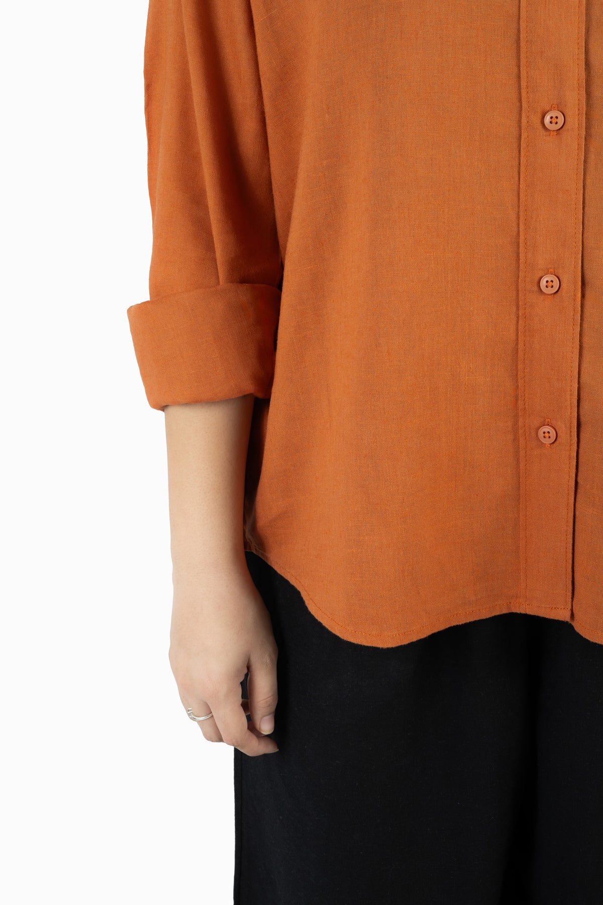 Close-up of a person wearing a rust-orange button-front top with rolled sleeves and black bottoms against a plain white background.