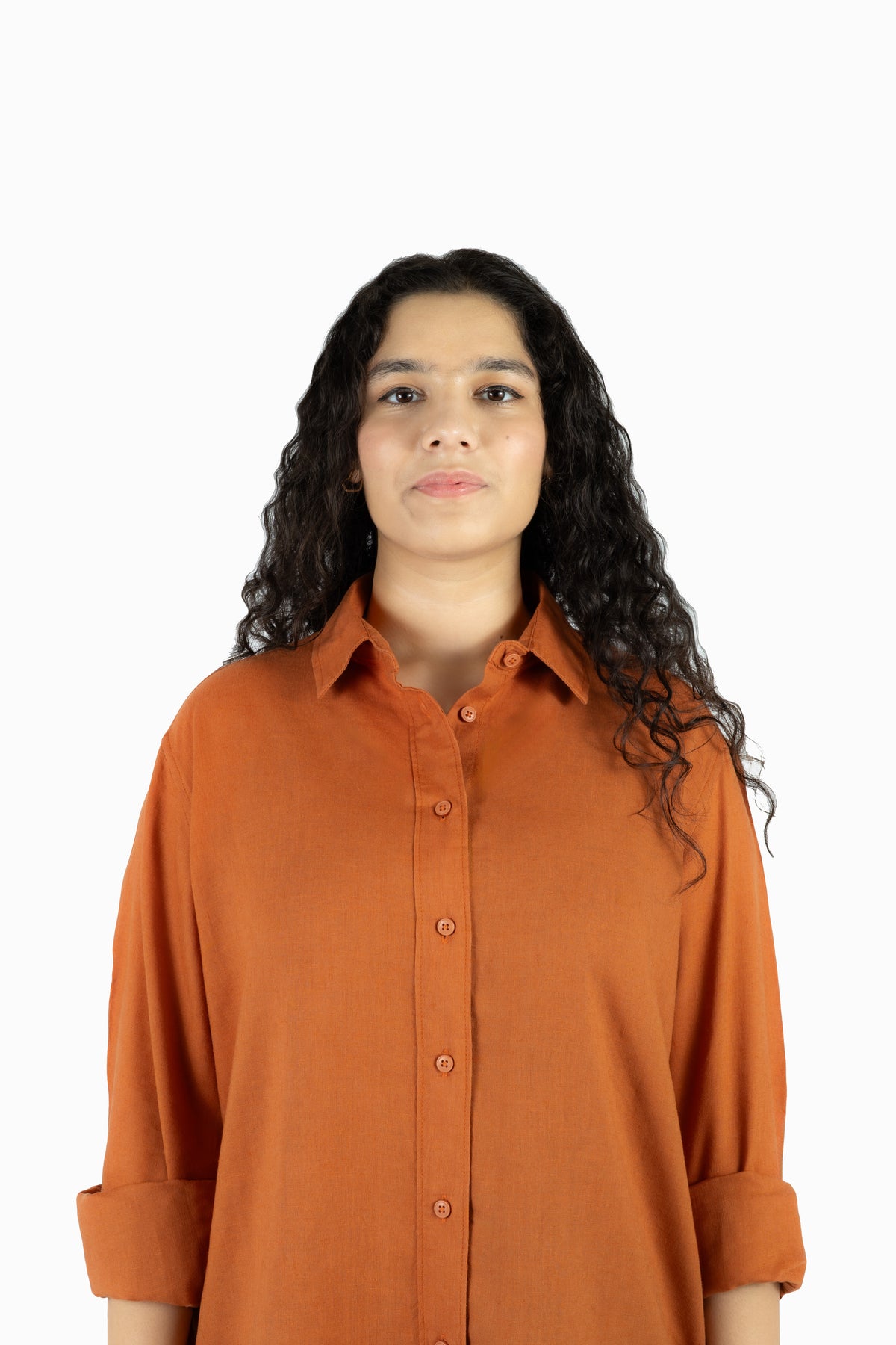 A woman with long, curly dark hair wearing a rust-orange button-down shirt, photographed against a solid white background.