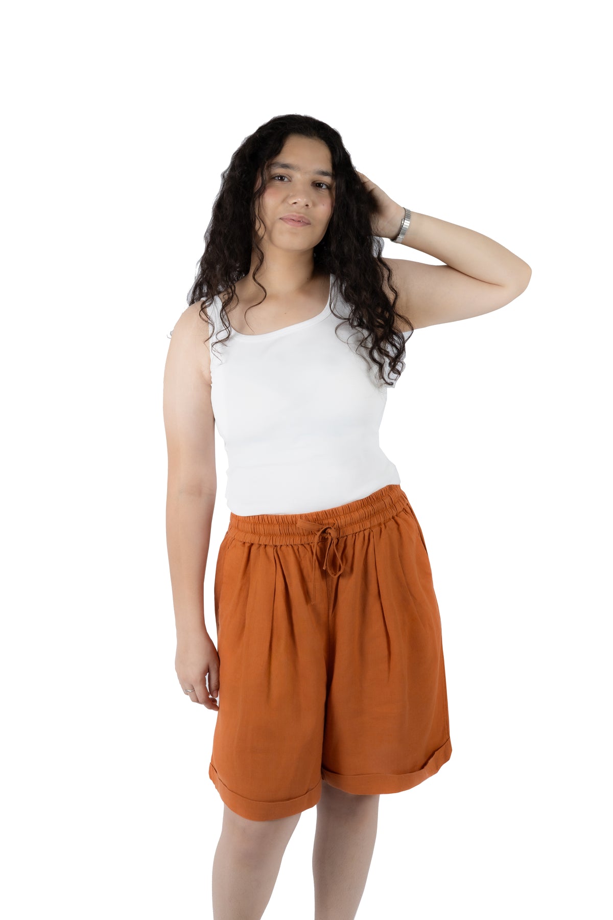 A woman modeling a pair of rust-orange drawstring shorts and a white tank top against a solid white background.