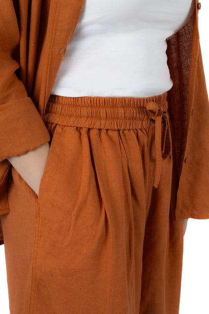 A close-up of a person wearing rust-orange wide-leg trousers with an elastic drawstring waist, styled with a white top and an open rust-orange cardigan.