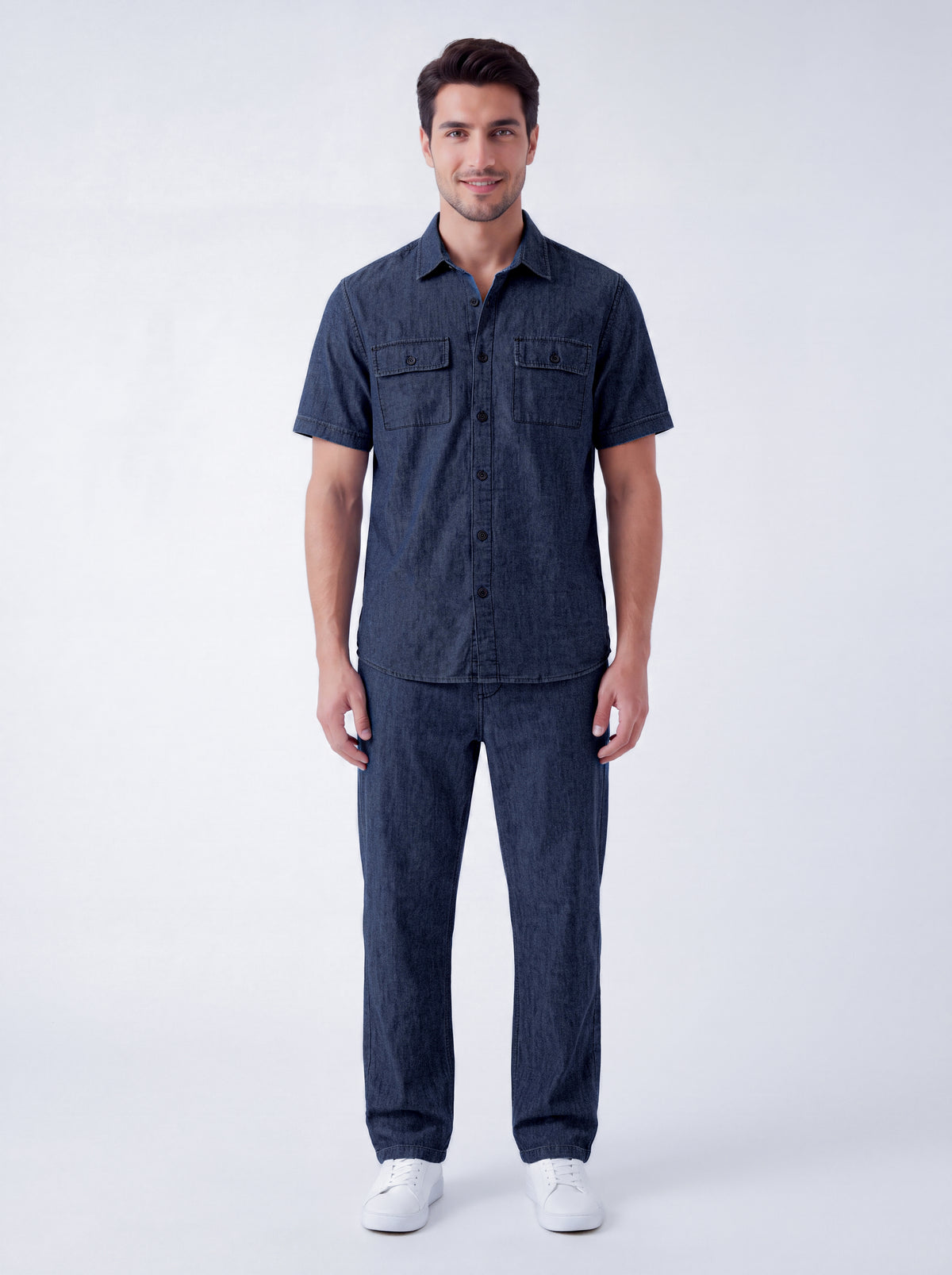 A man modeling a dark navy blue short-sleeve button-up shirt and matching navy blue jeans, standing against a light gray studio background.
