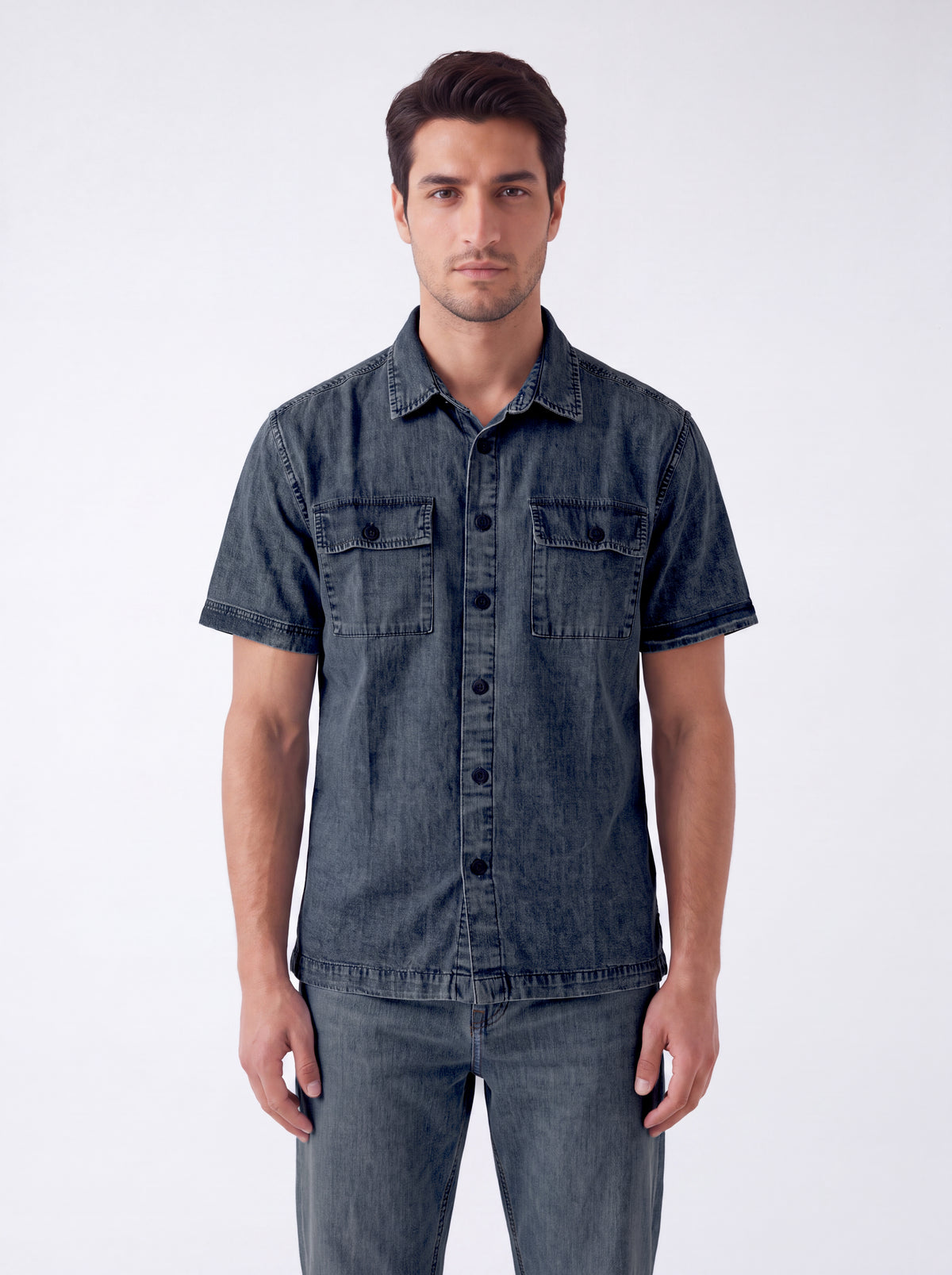 A man wearing a dark gray washed denim short-sleeve button-up shirt and matching gray jeans, standing against a light gray studio background.