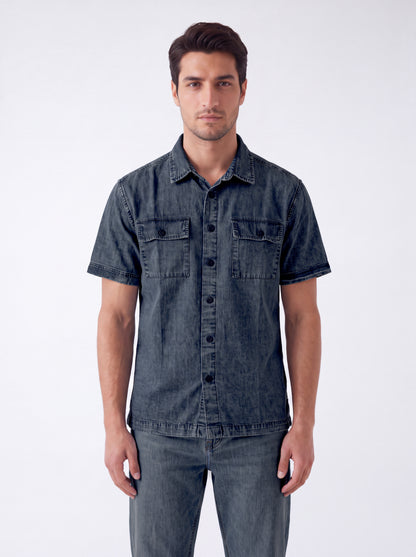 A man wearing a dark gray washed denim short-sleeve button-up shirt and matching gray jeans, standing against a light gray studio background.