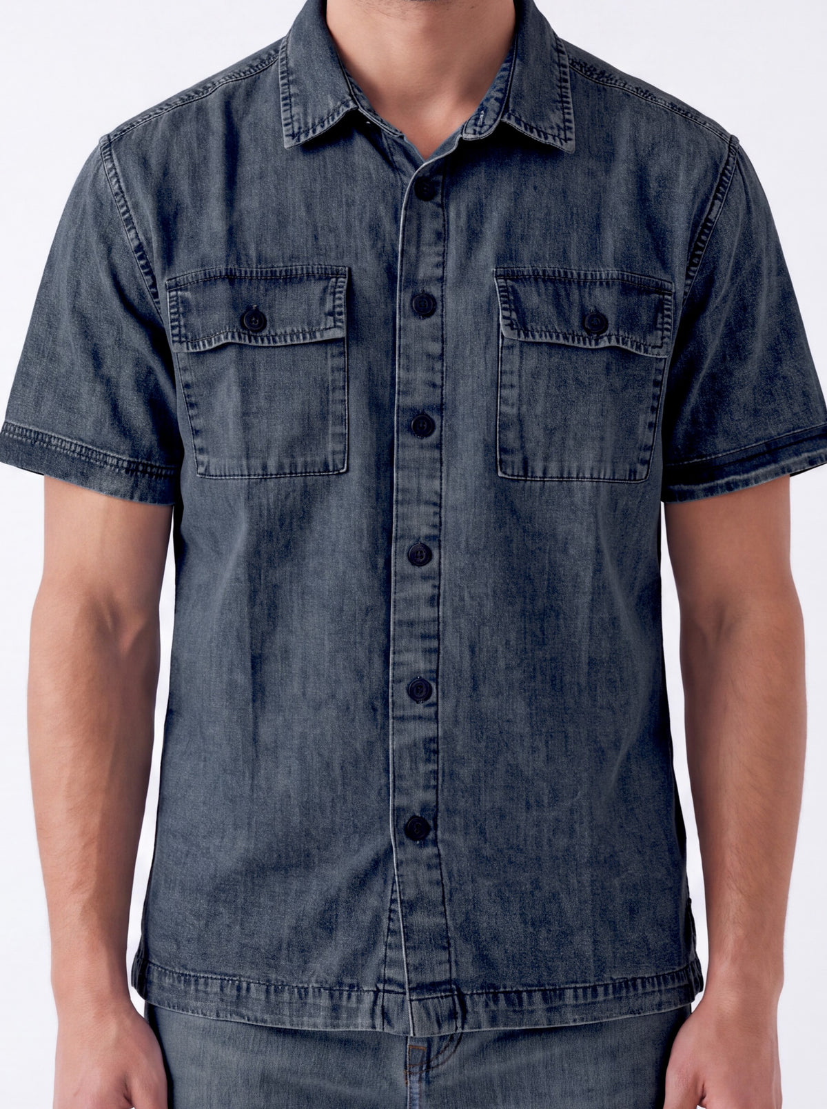 A man wearing a dark blue denim short-sleeve button-up shirt with two chest pockets, shown from the neck down against a plain white background.
