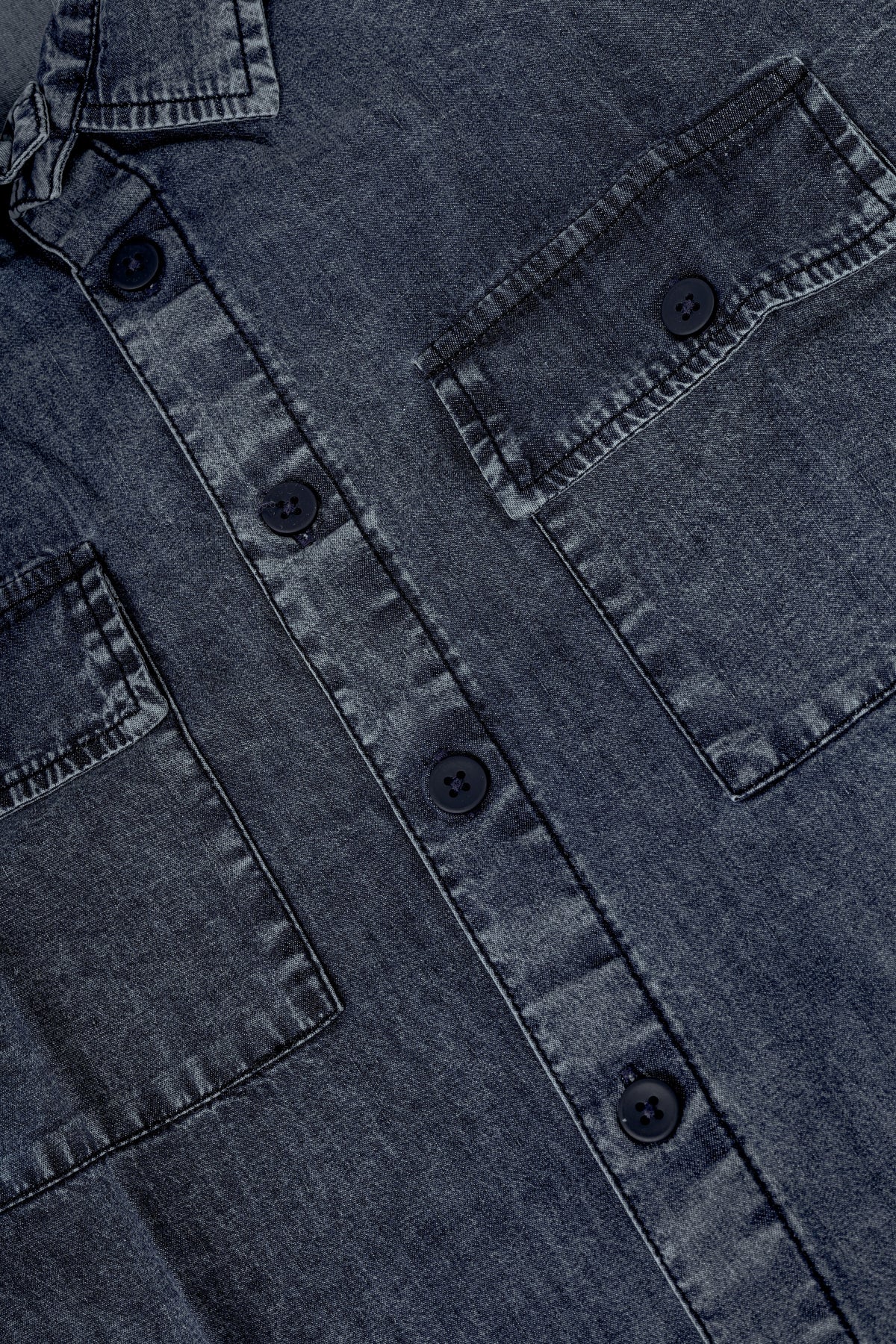 Close-up of a dark washed denim button-up shirt showing the chest pocket, button closure, and fabric texture.