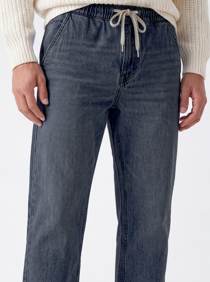 A close-up of a person wearing dark blue denim drawstring pants with a cream ribbed knit sweater, shown from the waist down against a plain white background.