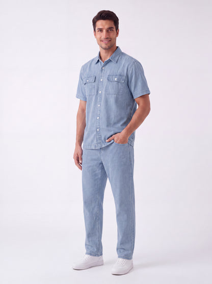 A man modeling a light blue denim short-sleeve button-up shirt and matching light blue denim jeans, paired with white sneakers, against a plain white studio background.