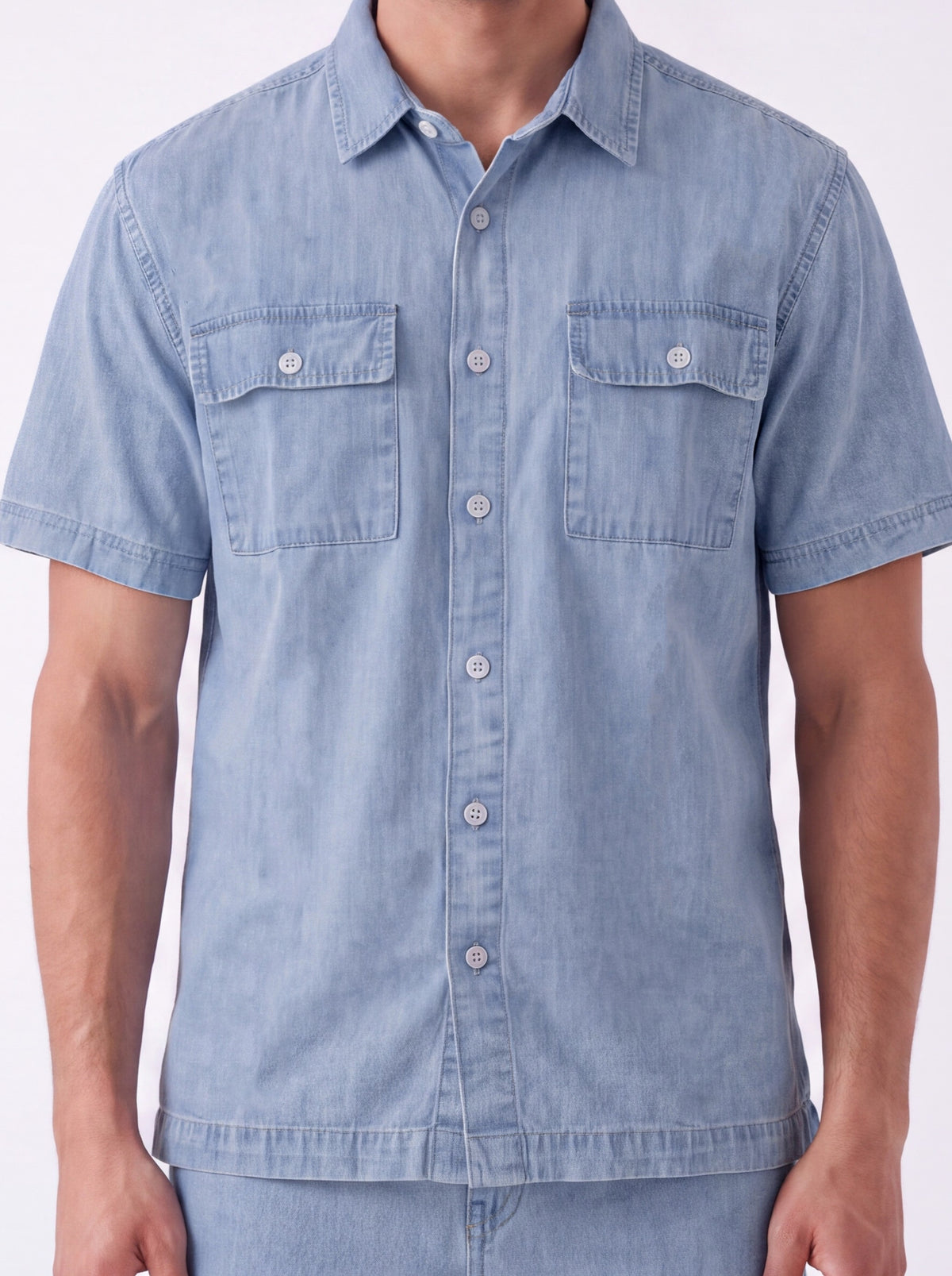 A man wearing a light blue short-sleeve button-up shirt with two chest pockets, shown from the neck down against a plain white background.