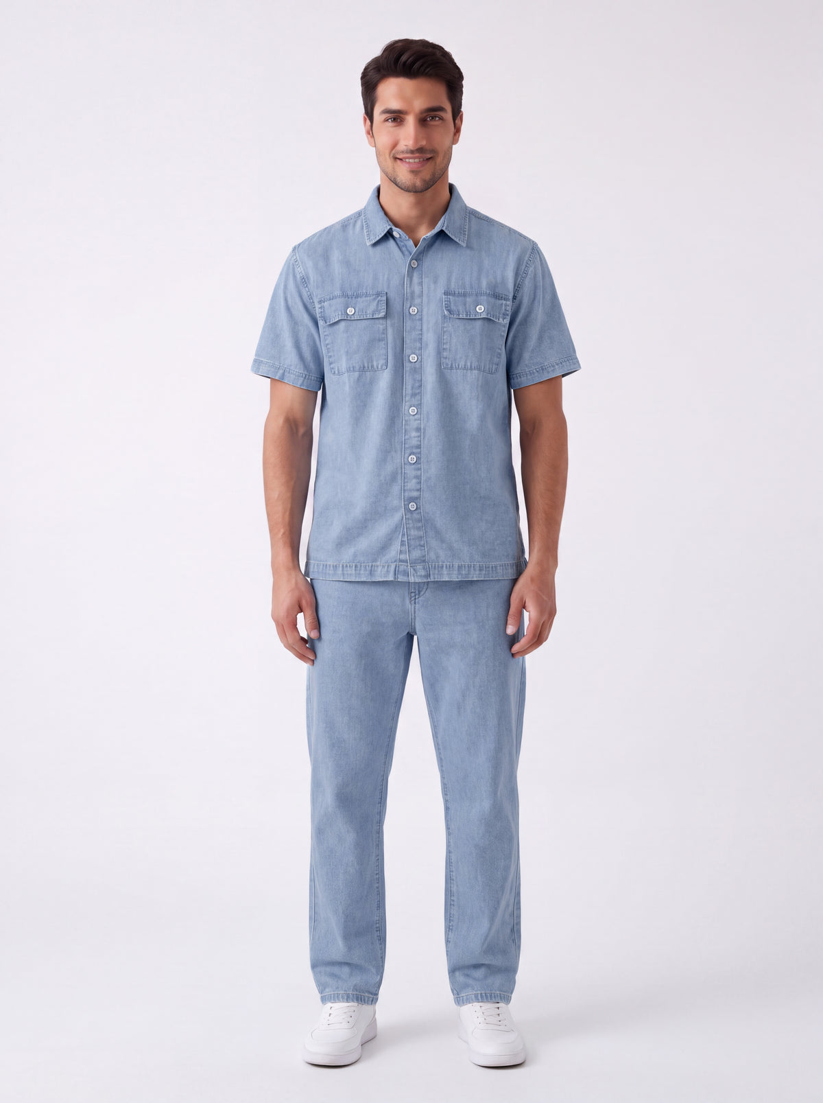 A man modeling a light blue denim short-sleeve button-up shirt and matching light blue denim jeans, paired with white sneakers, against a plain white studio background.