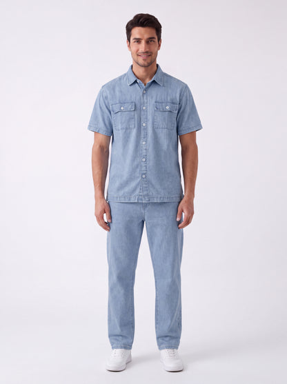 A man modeling a light blue denim short-sleeve button-up shirt and matching light blue denim jeans, paired with white sneakers, against a plain white studio background.