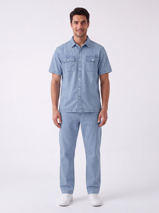 A man modeling a light blue denim short-sleeve button-up shirt and matching light blue denim jeans, paired with white sneakers, against a plain white studio background.